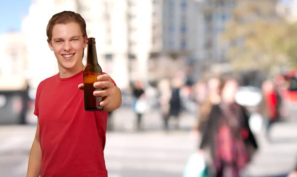 Retrato de jovem segurando cerveja na rua lotada — Fotografia de Stock