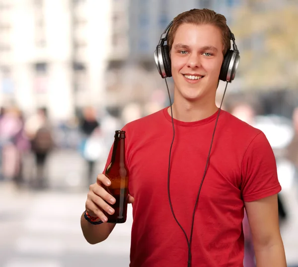 Retrato de un joven escuchando música y sosteniendo cerveza contra un —  Fotos de Stock