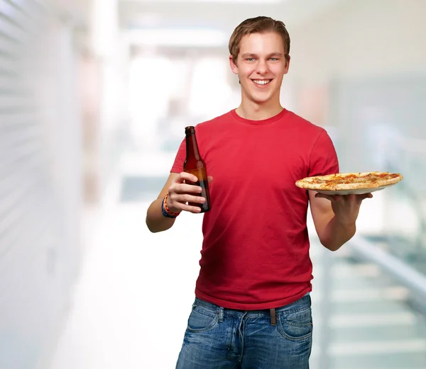 Portret van jonge man houden pizza en bier binnen — Stockfoto