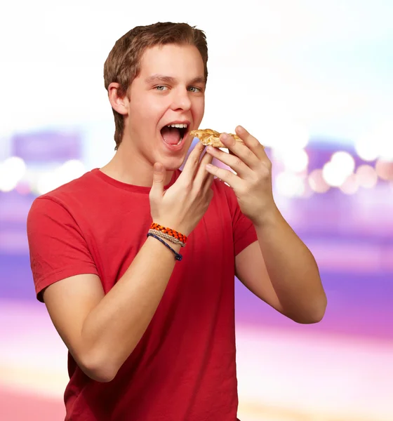 Ritratto di un giovane che mangia pizza su uno sfondo astratto — Foto Stock