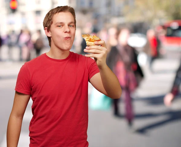 Porträt eines jungen Mannes, der an einer belebten Straße Pizza isst — Stockfoto