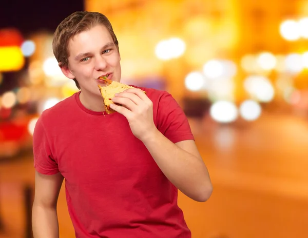 Portrait d'un jeune homme mangeant une pizza la nuit en ville — Photo