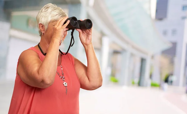 Uma mulher sênior olhando através de binóculos — Fotografia de Stock