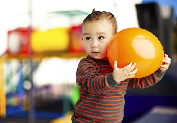 Porträt eines lustigen Kindes, das einen großen orangefarbenen Luftballon gegen einen Bauch hält — Stockfoto