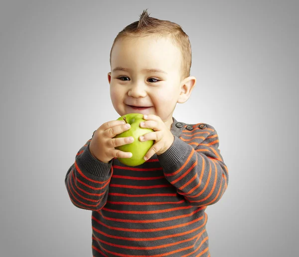 Portrait of funny kid holding green apple and smiling over grey — Stock Photo, Image