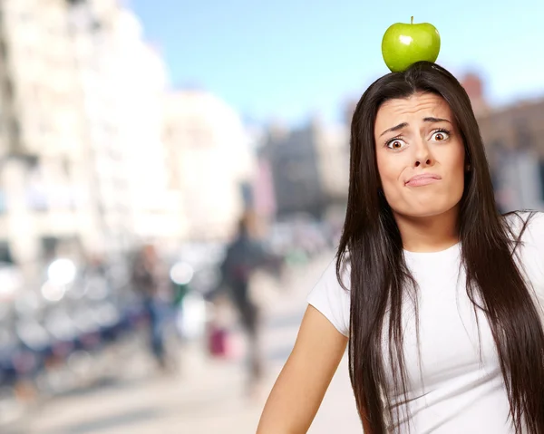 Портрет молодой женщины, держащей зеленое яблоко на голове у толпы — стоковое фото