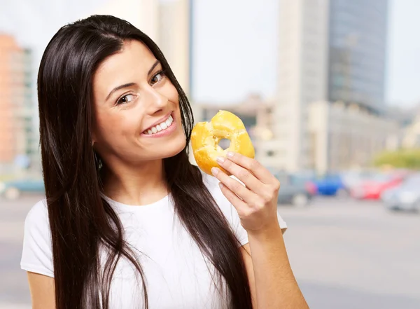 Portræt af ung kvinde, der spiser en donut i storbyen - Stock-foto