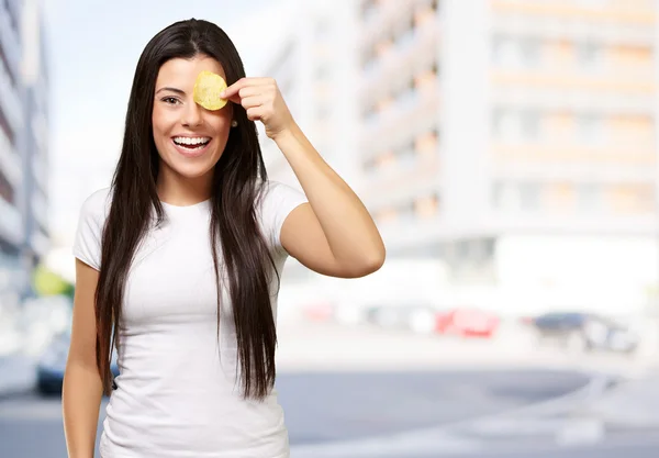 Portrait of young woman holding a potato chip in front of her ey — Stock Photo, Image