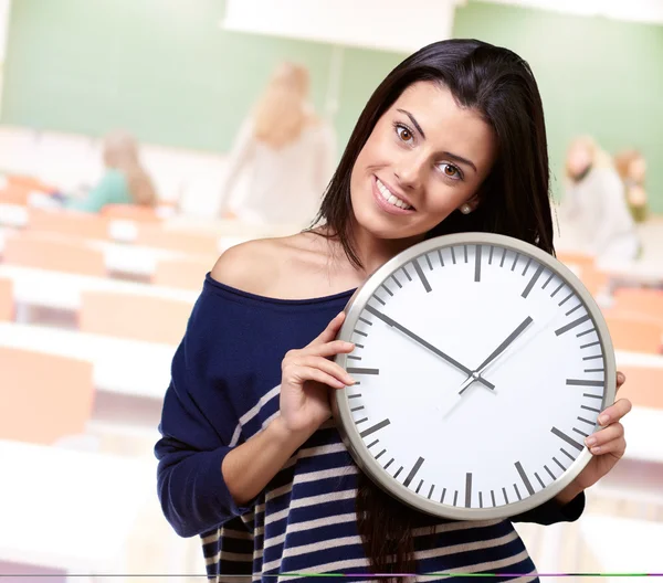 Retrato de una mujer joven sosteniendo el reloj en el aula — Foto de Stock