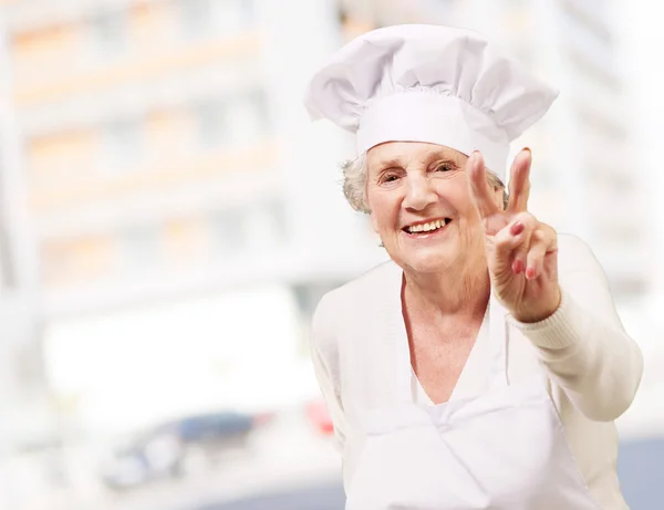Portrait of cook senior woman doing good gesture against a moder Stock Photo