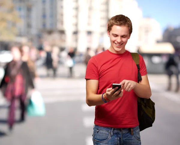 Porträt eines jungen Mannes, der Handy-Bildschirm an belebter Straße berührt Stockbild
