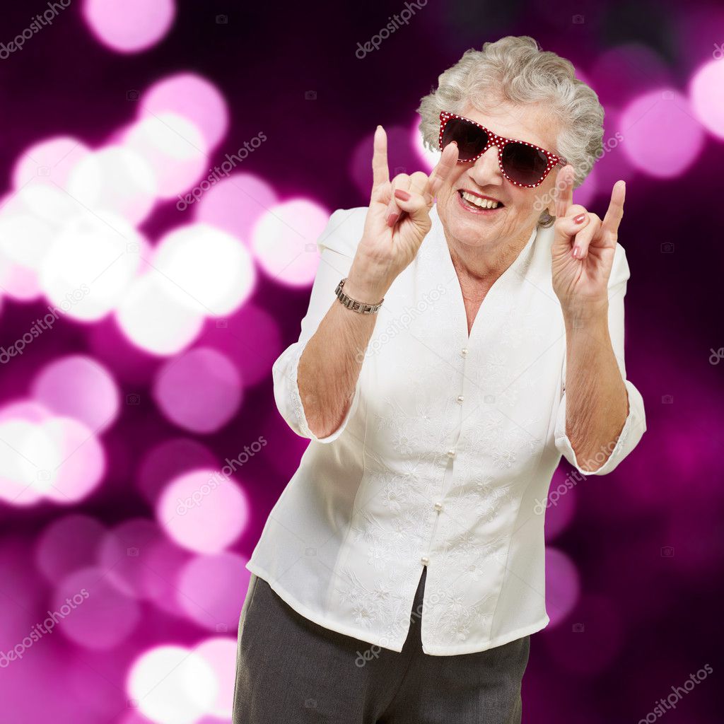 Portrait of a happy senior woman doing rock symbol against a abs