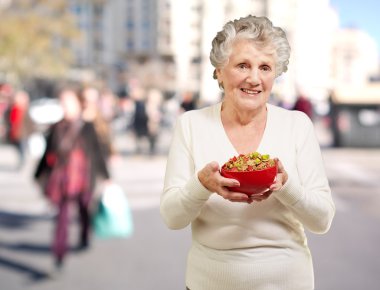 Portrait of healthy senior woman holding cereals bowl at street clipart