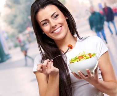 Portrait of healthy woman eating salad at city clipart