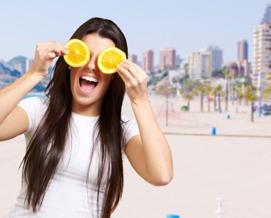 Portrait of young woman holding orange slices in front of her ey clipart