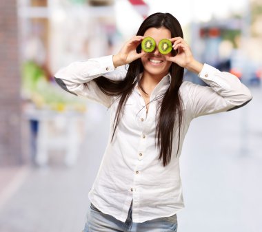 Portrait of young girl holding kiwi slices in front of her eyes clipart