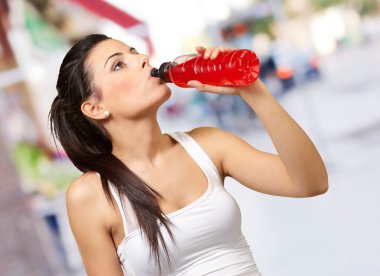 Portrait of young sporty woman drinking isotonic drink at street clipart