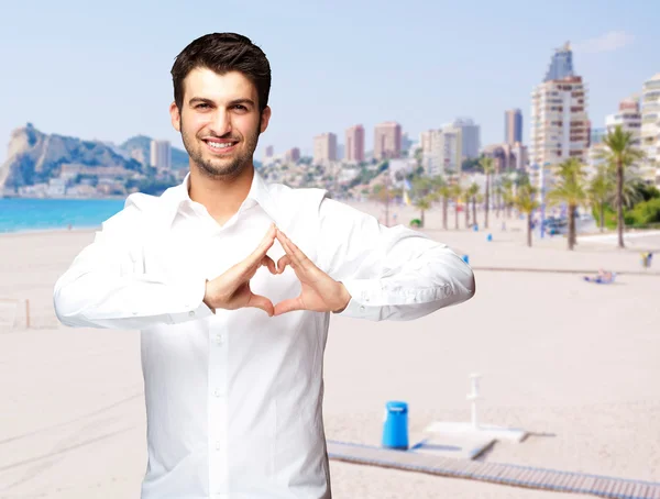 Porträtt av ung man gör hjärtsymbol mot en strand — Stockfoto