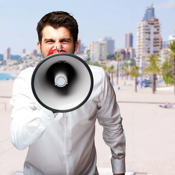Portrét mladého muže, překypující megafon proti pláži — Stock fotografie