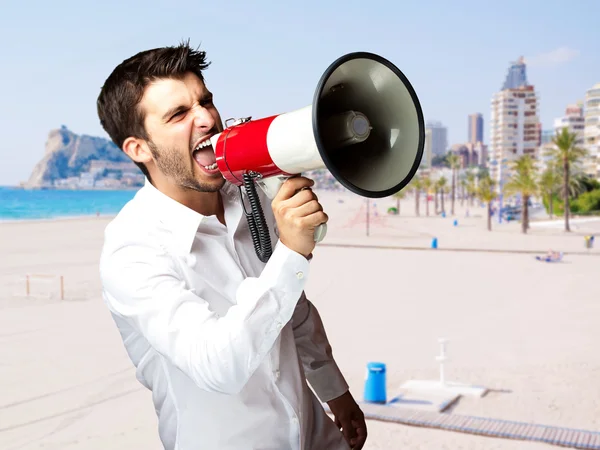Portret van jonge man schreeuwen met megafoon tegen een strand — Stockfoto