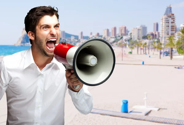 Ritratto di un giovane che urla con un megafono contro una spiaggia — Foto Stock