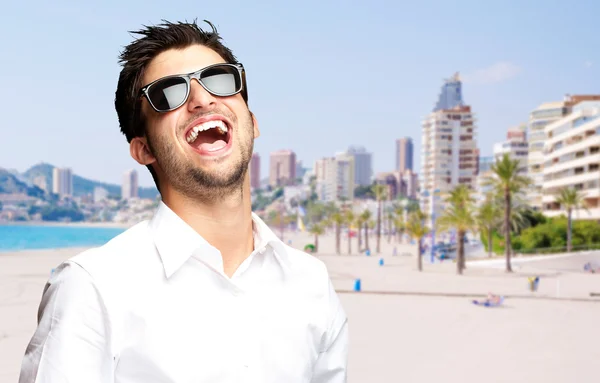 Portret van een vrolijke jonge man tegen een strand — Stockfoto