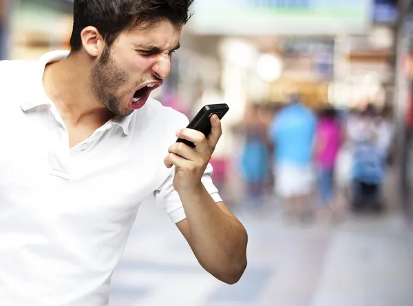Retrato de un joven enojado gritando usando el móvil a una m concurrida — Foto de Stock