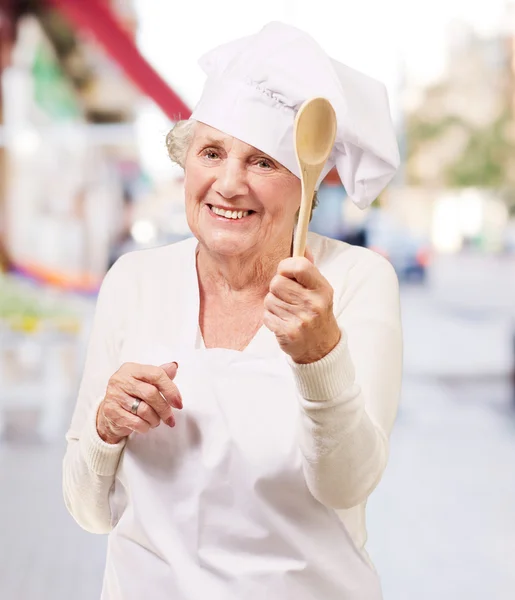 Portret kobiety starszy kucharz trzyma drewnianą łyżką na ulicy — Zdjęcie stockowe