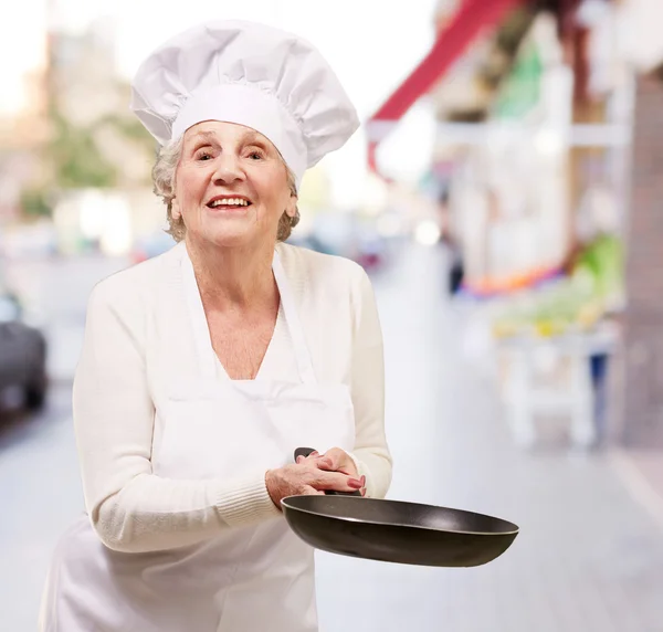 Портрет дружелюбной повара пожилой женщины, держащей сковородку в городе — стоковое фото
