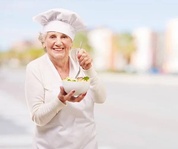Retrato de adorable cocinera senior comiendo ensalada en la calle — Foto de Stock