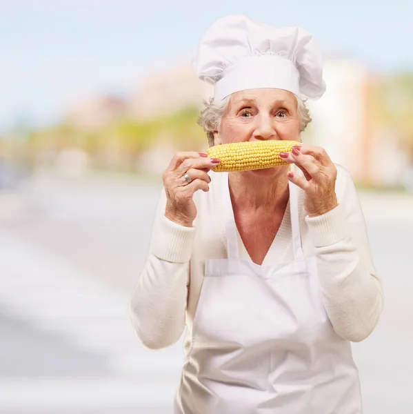 Retrato de cocinera mujer mayor comiendo mazorca de maíz en la ciudad — Foto de Stock