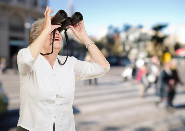 Porträtt av äldre kvinna som tittar genom en kikare på trångt — Stockfoto