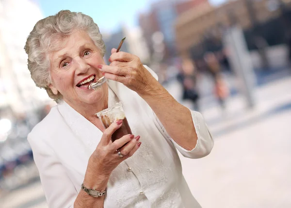 Portret senior kobiety jedzenie czekolady i krem kubek w stree — Zdjęcie stockowe