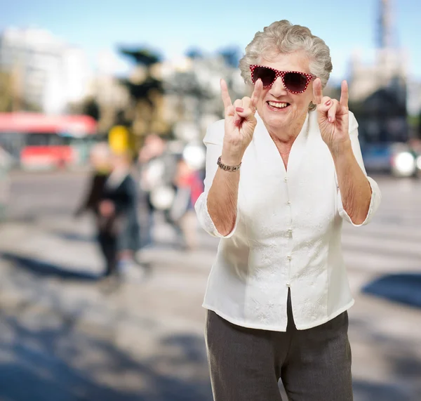 Портрет счастливой пожилой женщины, изображающей рок-символ на переполненной улице — стоковое фото