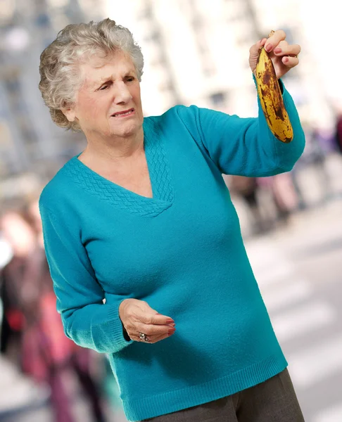 Senior woman holding a rotten banana at crowded street — Stock Photo, Image