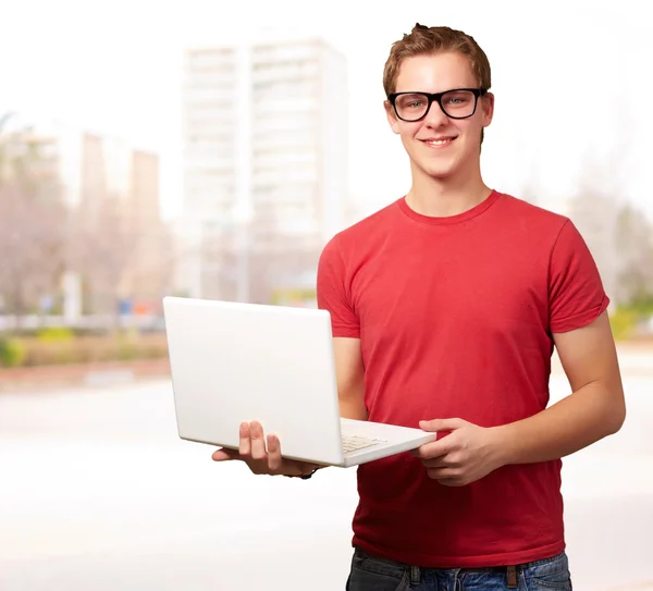 Retrato de un joven estudiante sosteniendo un ordenador portátil contra un paisaje urbano —  Fotos de Stock