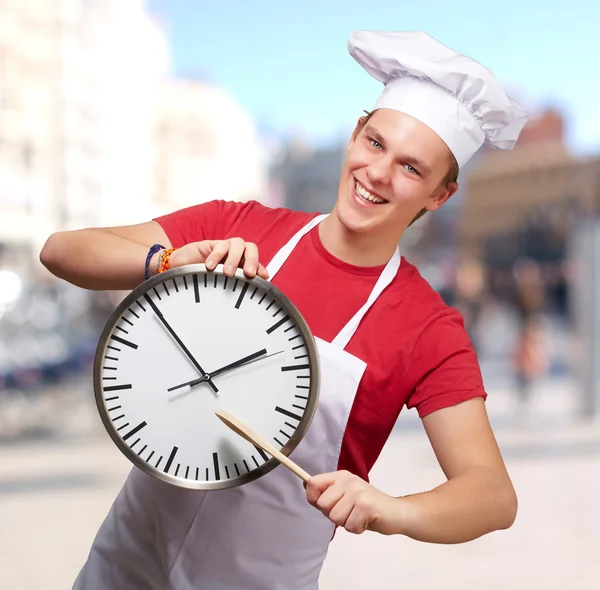 Portrait d'un jeune cuisinier pointant une horloge vers la rue — Photo