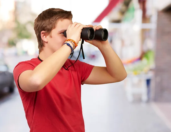 Portrait of young man looking through a binoculars at street — Stock Photo, Image