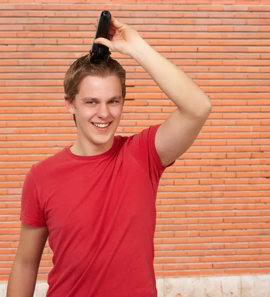 Portrait of young man cutting his hair against a bricks wall — Stock Photo, Image