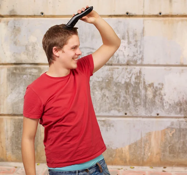 Portrait of young man cutting his hair against a street wall — Stock Photo, Image