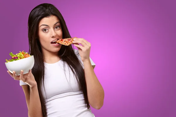 Kvinnliga äta en bit av pizza och hålla en salladsskål女性のピザの部分を食べることとサラダ ボウルを保持 — ストック写真