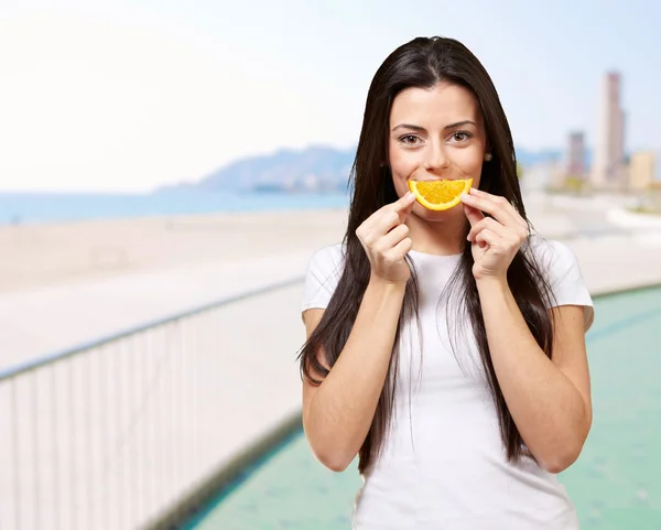 Retrato de mulher jovem segurando fatia de laranja contra uma praia — Fotografia de Stock