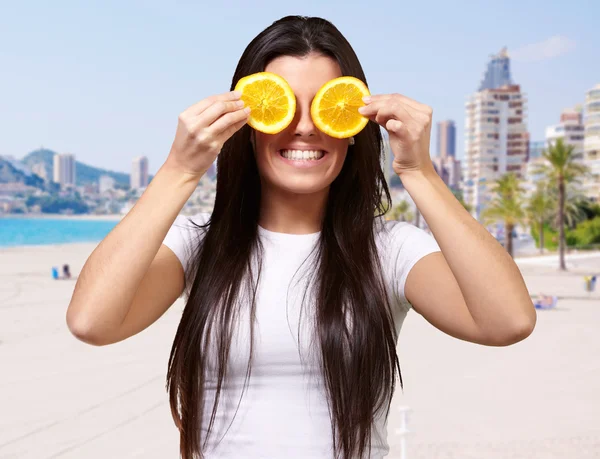 Portrait of young woman holding orange slices in front of her ey — Stock Photo, Image