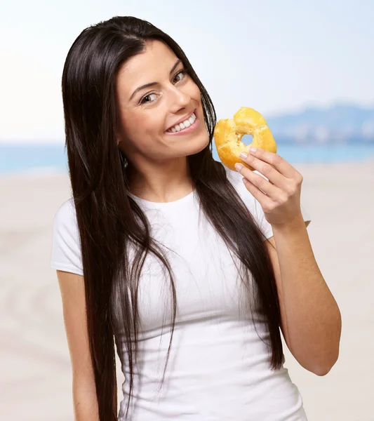 Portrait of young woman holding donut against the beach — Stock Photo, Image