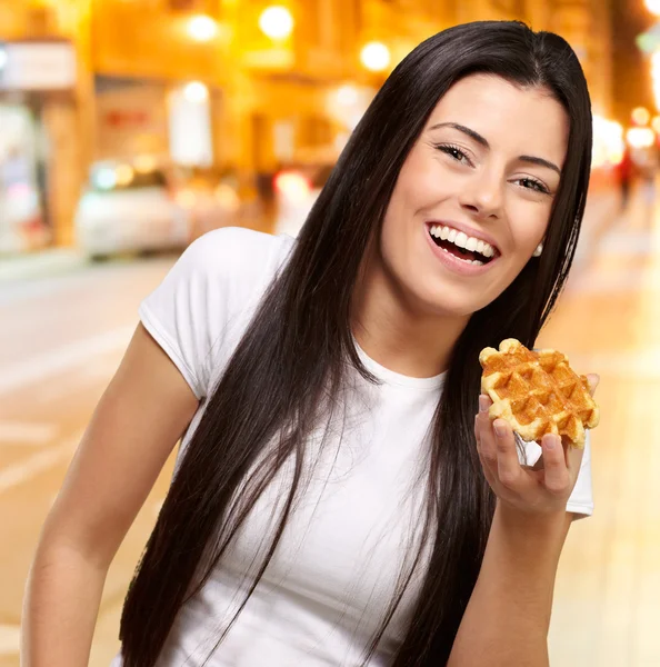 Portrait of young woman holding waffle at night city — Stock Photo, Image