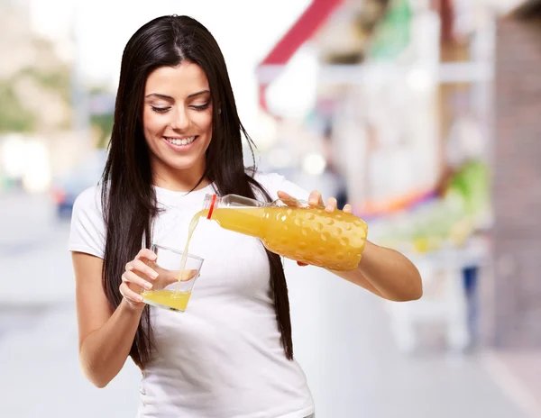 Portrait of young woman pouring orange juice on glass at city — Stock Photo, Image