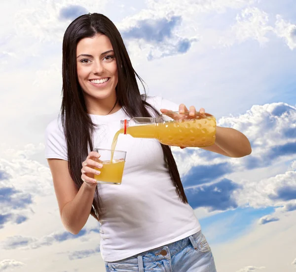 ガラスのオレンジ ジュースを注いで若い女性の肖像画 — ストック写真