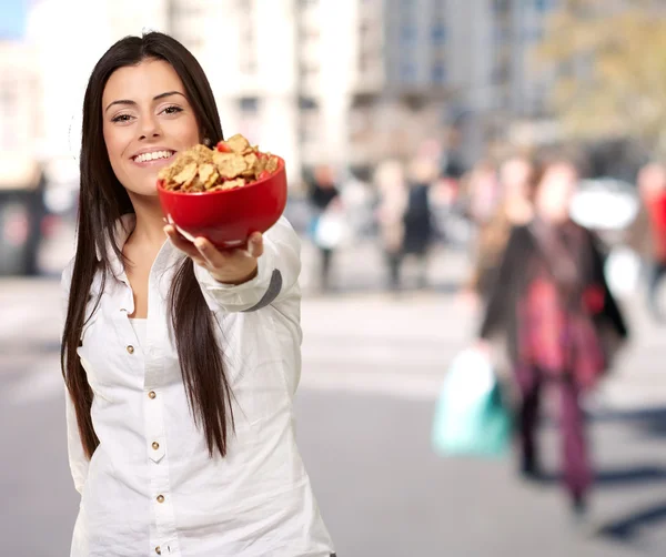 Retrato de jovem mulher oferecendo tigela de cereais na rua lotada — Fotografia de Stock