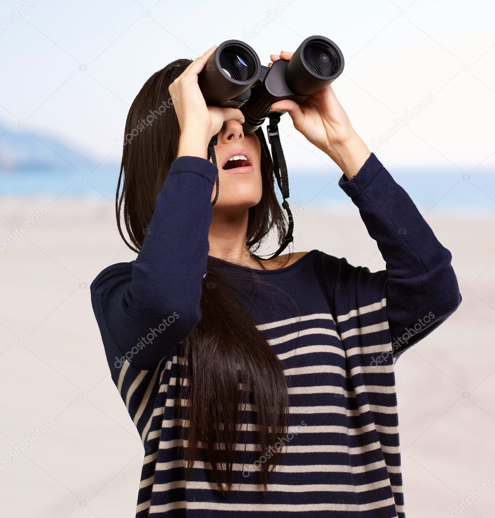 Portrait of young woman looking through a binoculars against a b