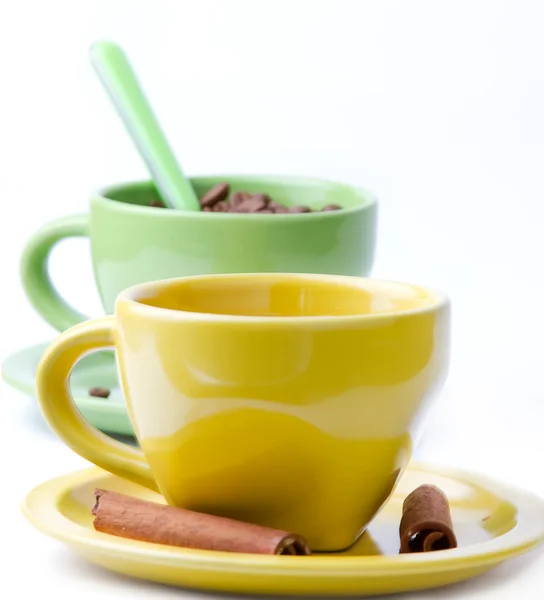 Grön och gul kopp med kaffebönor och två kanelstänger — Stockfoto